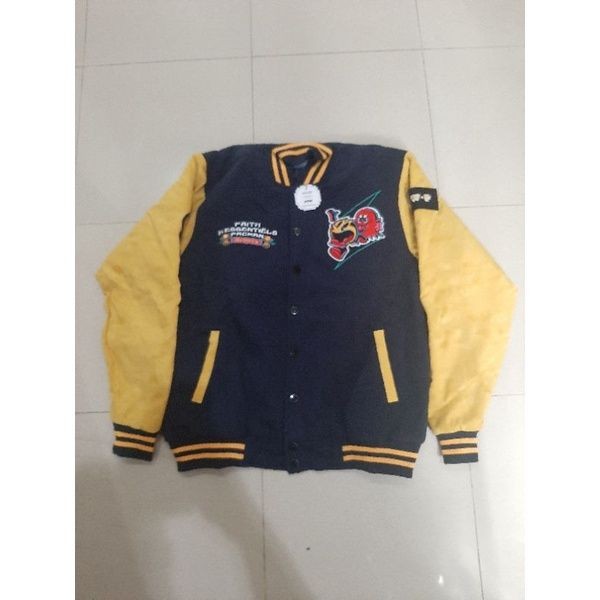 Navy blue and yellow varsity jacket with embroidered patches and buttons, displayed on a tiled floor.