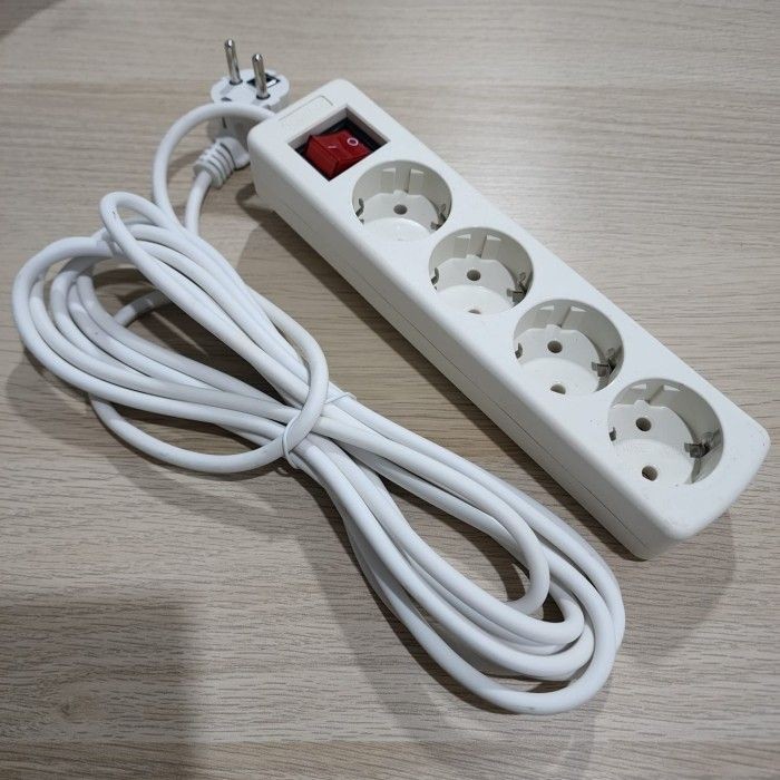 White power strip with four sockets and a red switch, coiled cable on a wooden surface.